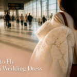 A bride holding a garment bag containing a wedding dress at an airport.