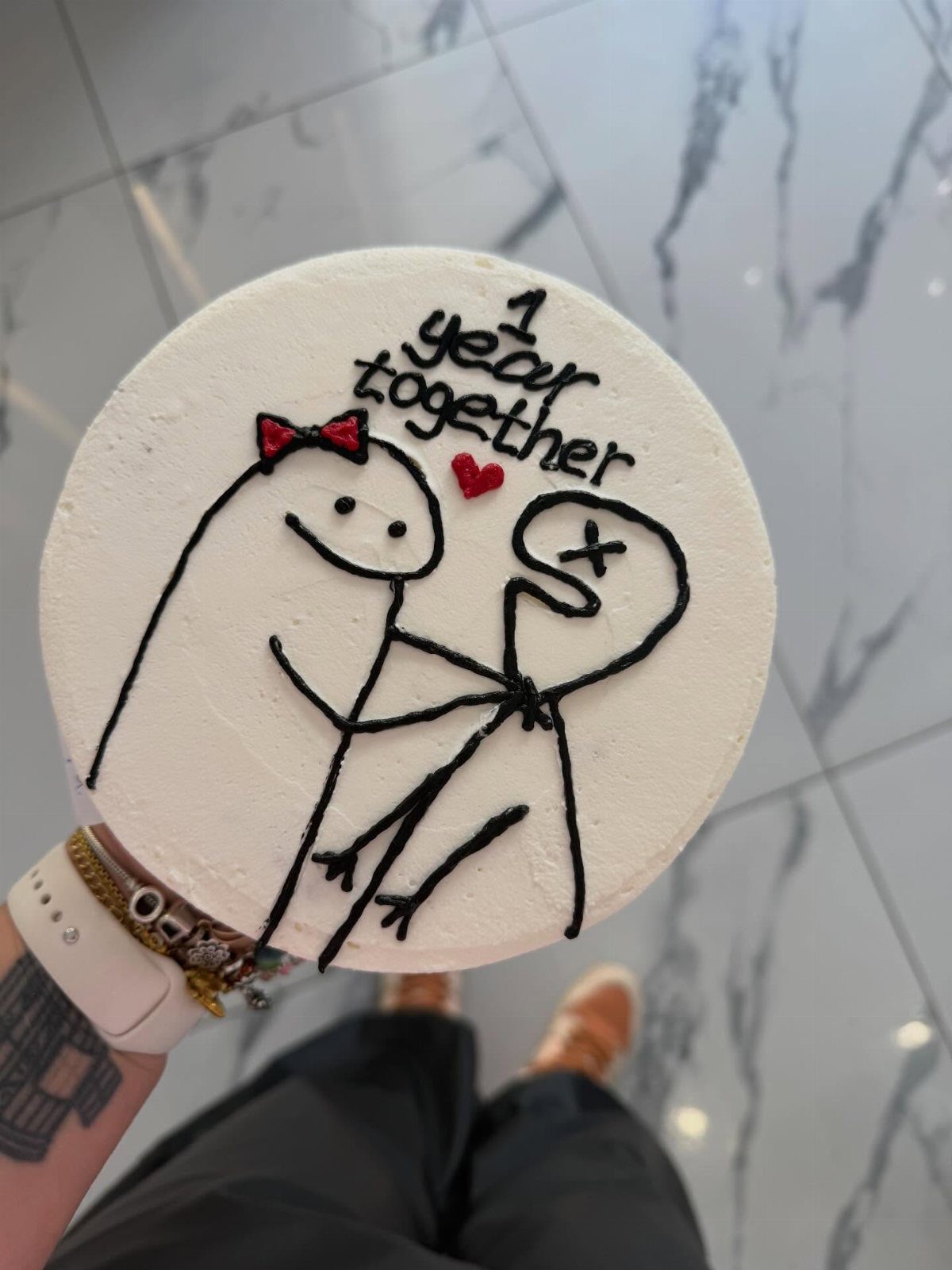 White frosted cake with stick figure drawings and 1 year together text