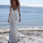 Woman in a white fit-and-flare sweetheart wedding dress with lace sleeves on a beach.