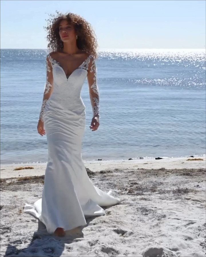 Woman in a white fit-and-flare sweetheart wedding dress with lace sleeves on a beach.
