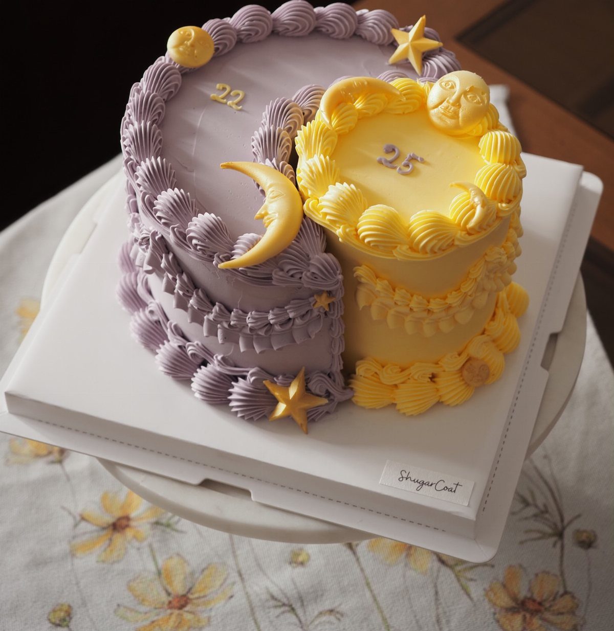 Two joined birthday cakes, one purple crescent and one yellow circle, with gold decorations.