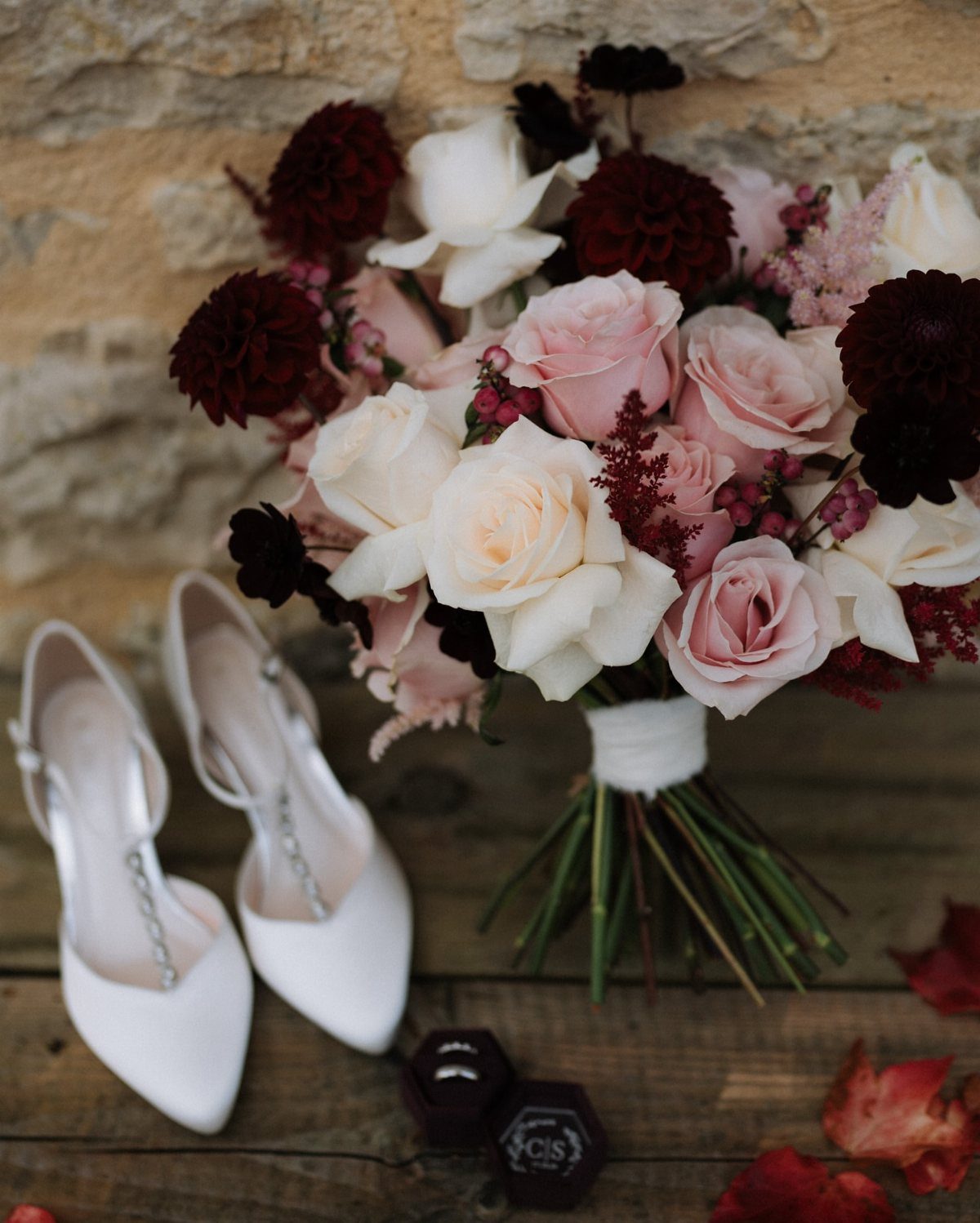 Blush and burgundy wedding flower bouquet next to white bridal shoes on wood.