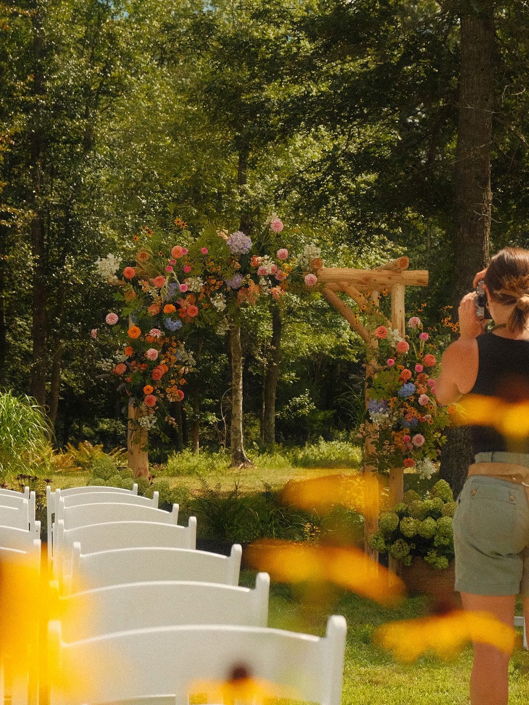 Wooden wedding trellis adorned with colorful flowers in a lush green forest setting.